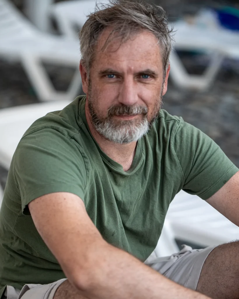 Man in his forties with a receding hairline, sitting outdoors in natural light