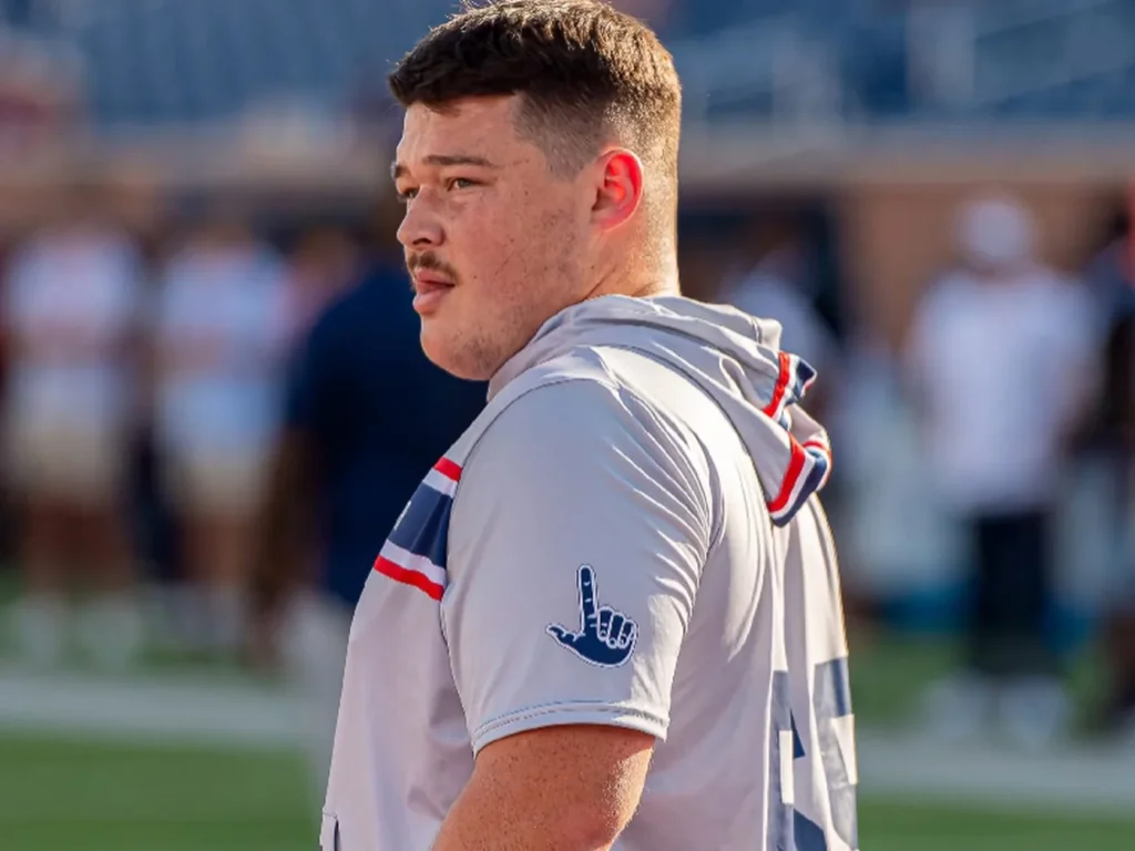 Sam on the sideline in warmup gear, looking out at the field
