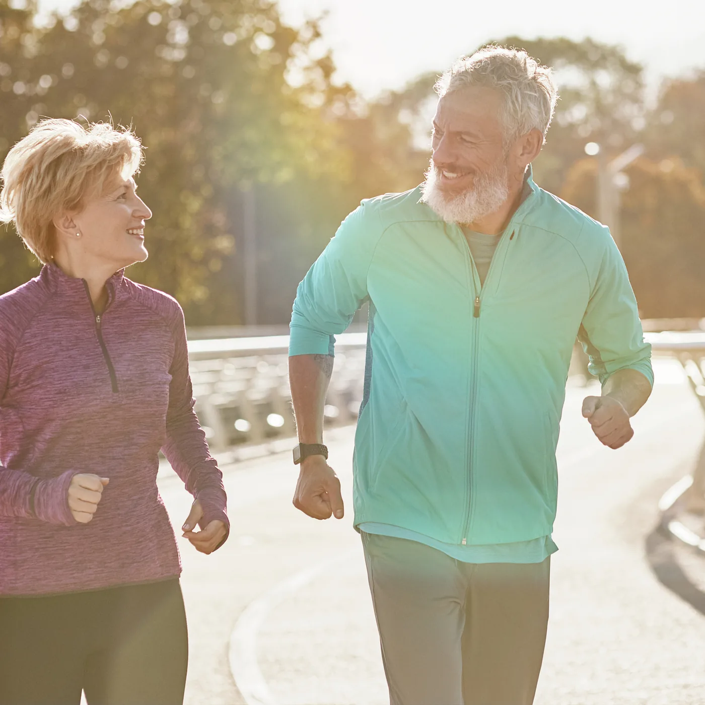 A man and a woman in their fifties running side by side on a boardwalk in morning light