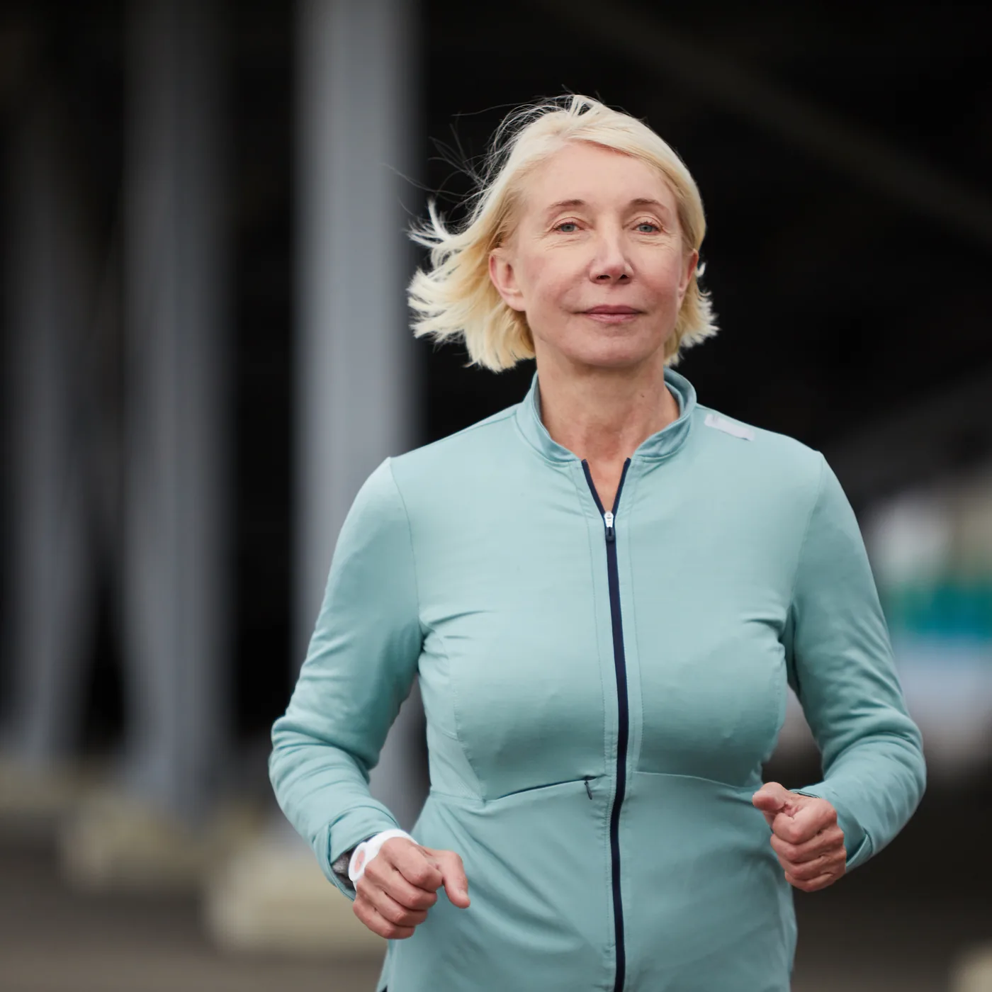 A woman in her fifties in a light blue jacket running under a bridge, calm and focused