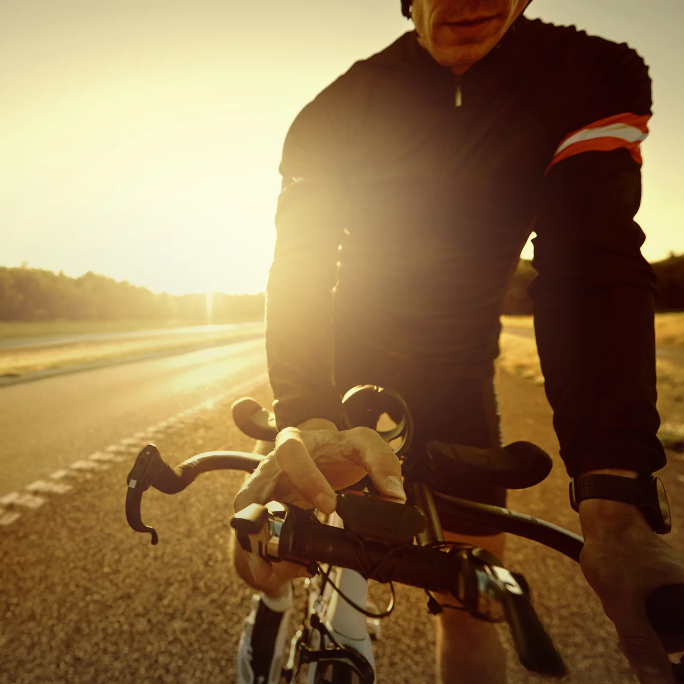 A cyclist on a road bike at sunrise, hands on the handlebars, face out of frame
